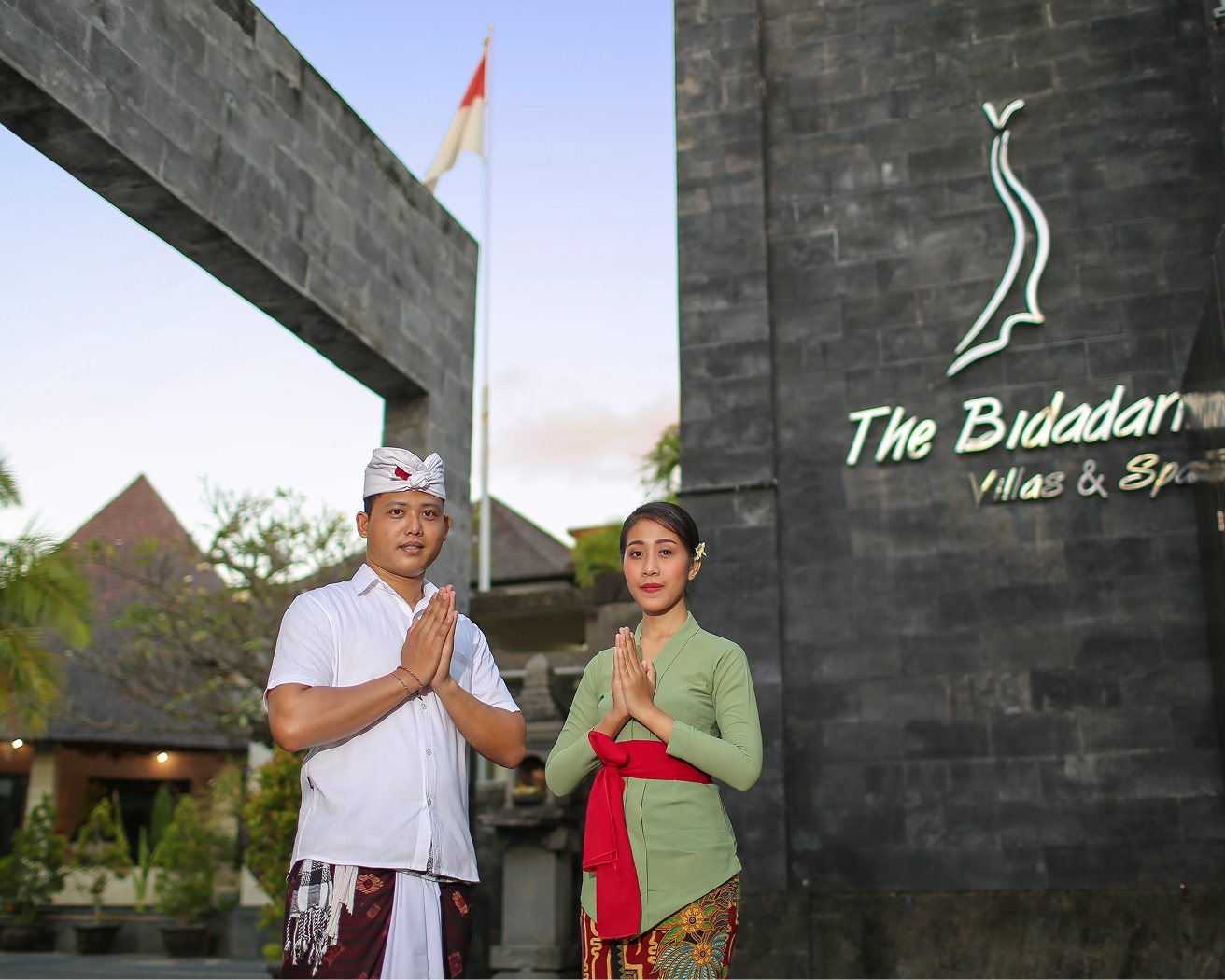 Couple in traditional Balinese attire at the entrance sign of The Bidadari Villas & Spa