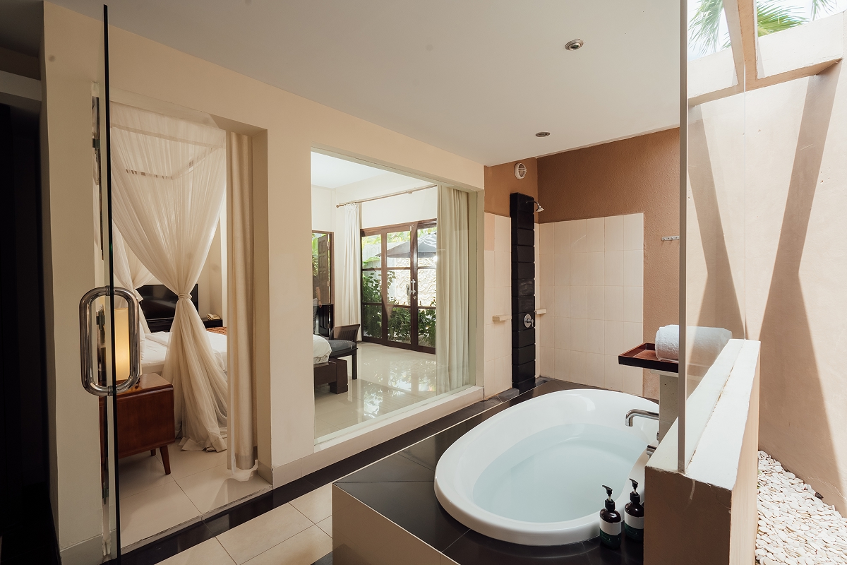 Bathroom with oval bathtub beneath a peaked thatched ceiling and stone wall, The Bidadari