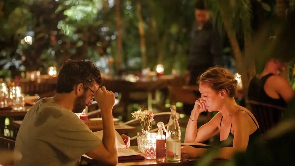 Couple enjoying an intimate candlelit dinner at a cozy outdoor restaurant.