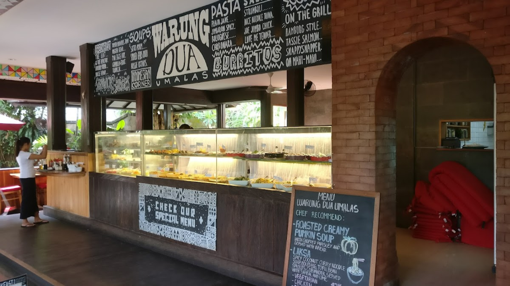 Casual restaurant counter displaying food beneath a large handwritten menu board.