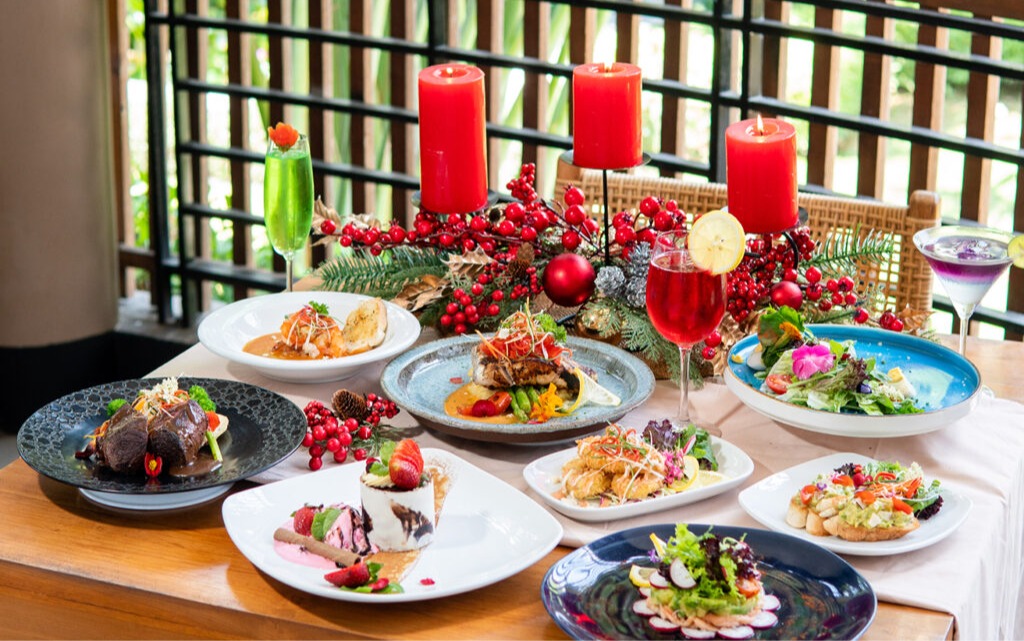 Festive dining table filled with colorful dishes, cocktails, red candles, and Christmas decorations.
