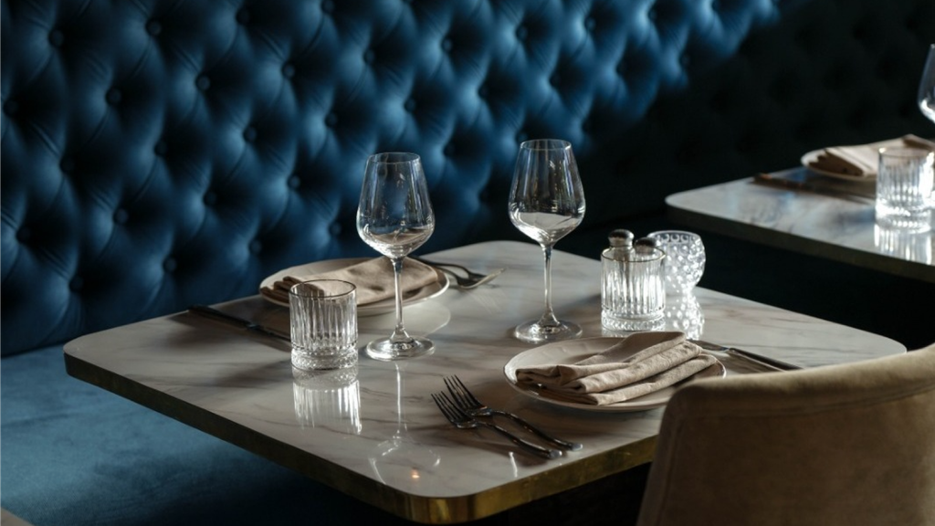 Elegant restaurant table set with wine glasses, plates, and glassware beside a blue upholstered booth.