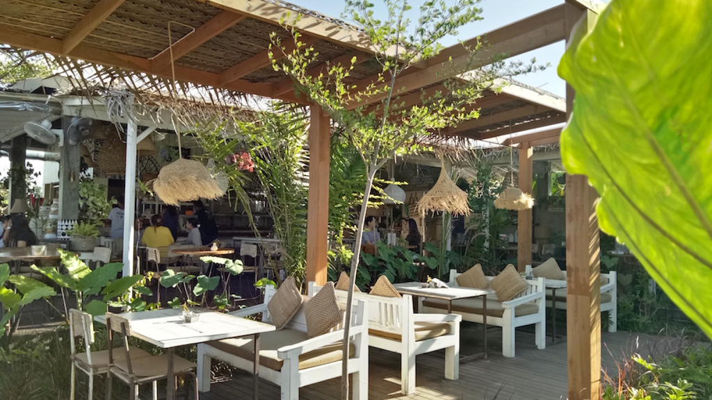 Tropical open air restaurant surrounded by lush greenery with wooden seating and natural decor.