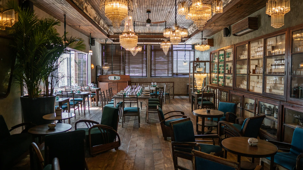 Stylish restaurant interior featuring wooden furniture, lush plants, and decorative chandeliers.