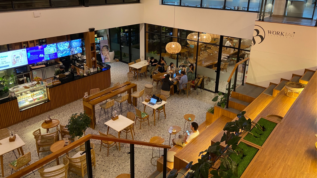 Modern coworking cafe with communal seating, warm wooden interiors, and people working and dining.